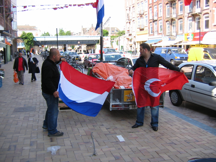 De Turkse en Nederlandse vlag samen in top. De foto is gemaakt op 16 juni in de Javastraat voor de winkel van Celal Yildiz. Samen met een medewerker hangt hij de Turkse en Nederlandse vlag op. De foto is gemaakt door de schrijver. 